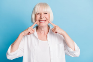 Woman smiling and pointing to her teeth on blue background