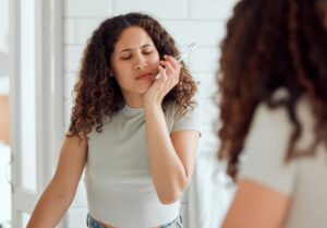 Woman holding jaw in pain while brushing. 