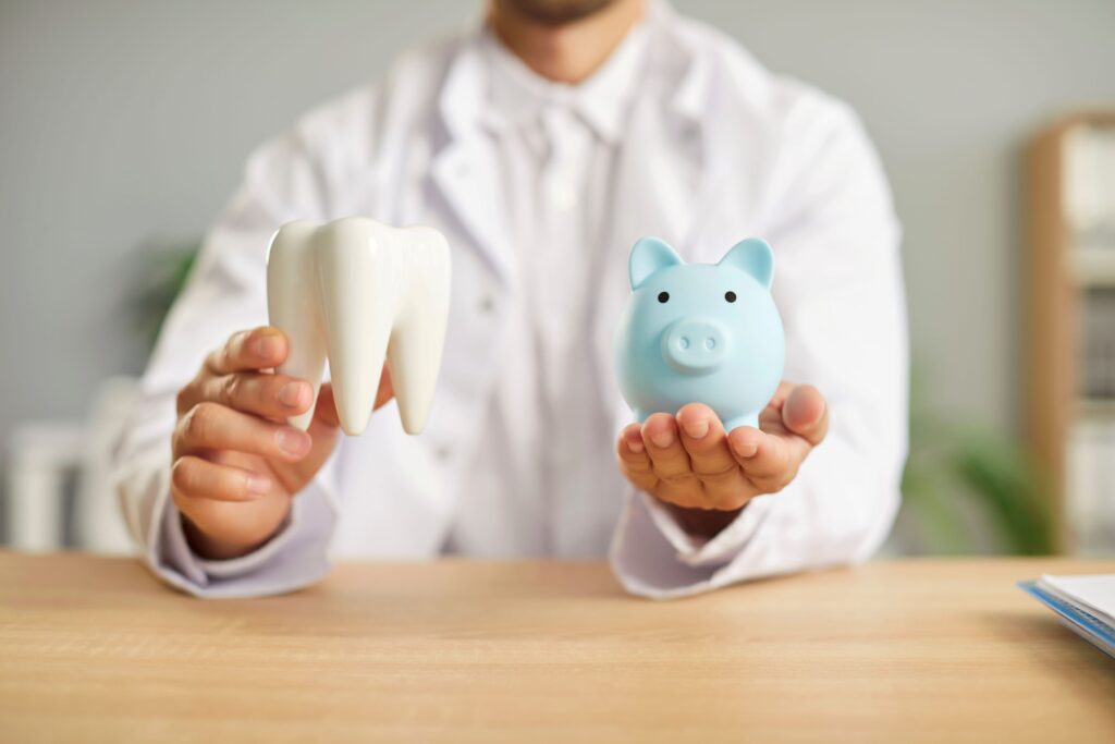Man in white coat holding large model tooth and blue piggy bank